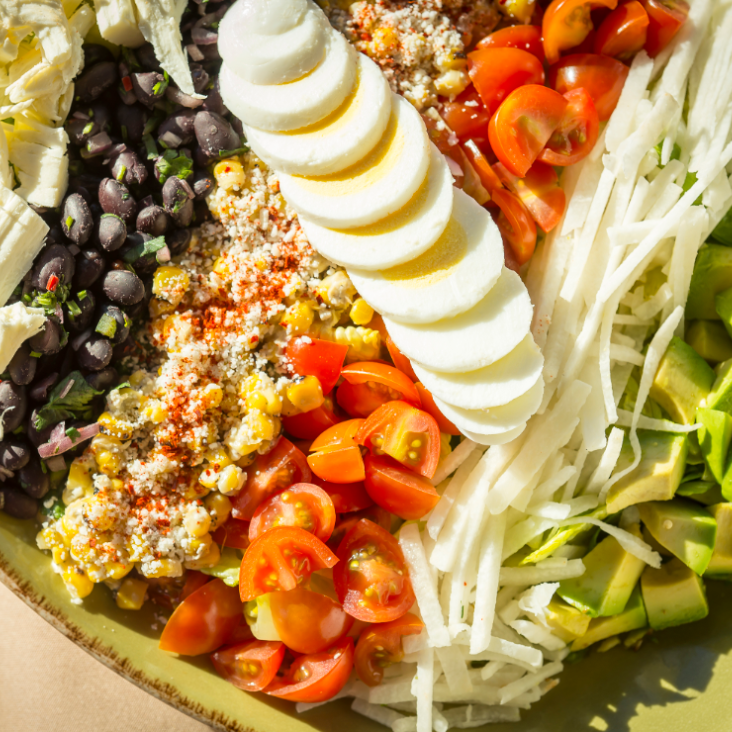 A colorful salad with sliced eggs, tomatoes, black beans, and corn.