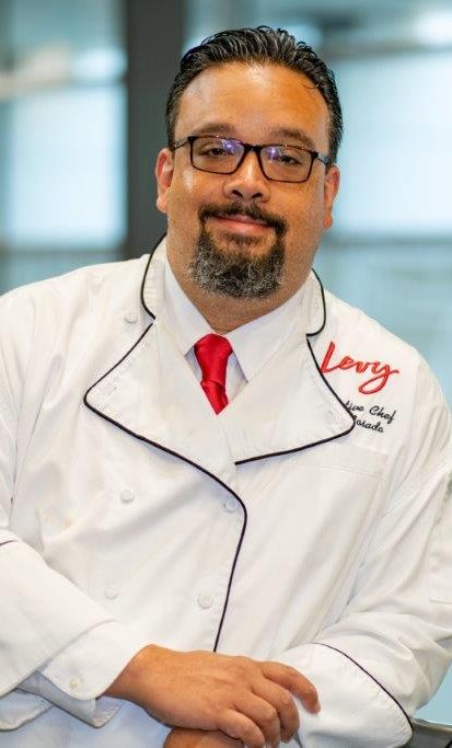 A smiling chef wearing a white jacket with a red tie.